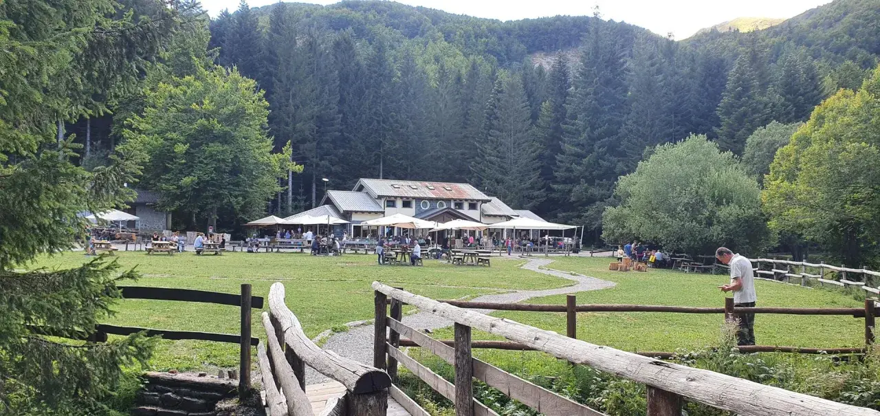 Un rifugio in Emilia Romagna immerso nel verde, con tavoli all'aperto e persone che si godono la giornata.