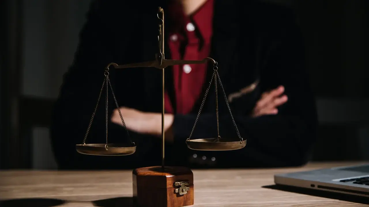 Bilancia della giustizia su un tavolo di legno, con una persona in giacca e camicia rossa sullo sfondo. Le ultime notizie sulla legge Pinto sono in arrivo.