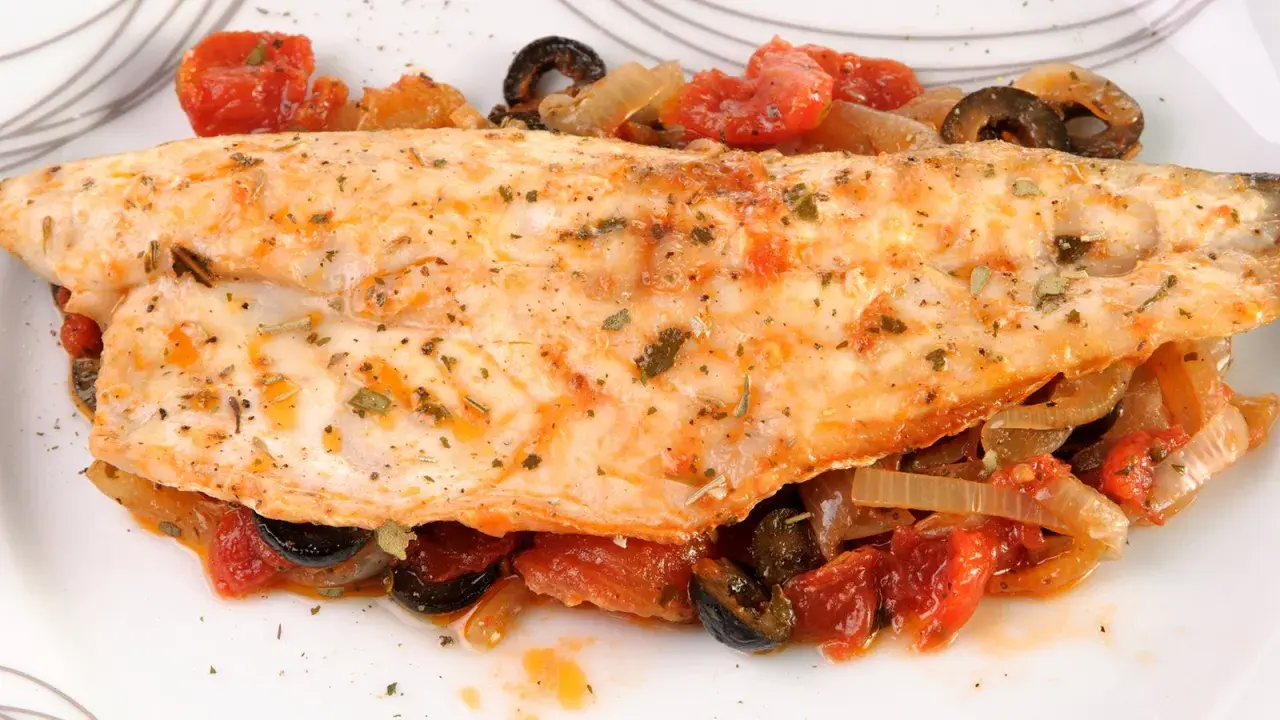 Leckerer Barsch zubereitet mit Tomaten, Zwiebeln und Oliven, garniert mit Kräutern. Ein Genuss für jeden Fischliebhaber.