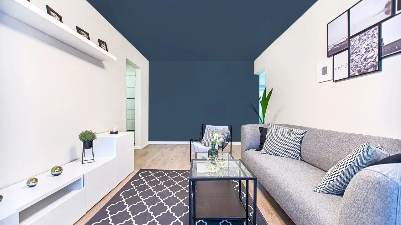 Un salon moderne avec un canapé gris, une table basse en verre et un tapis à motifs. Le plafond bleu foncé donne une impression de profondeur, une astuce pour comment agrandir une pièce.