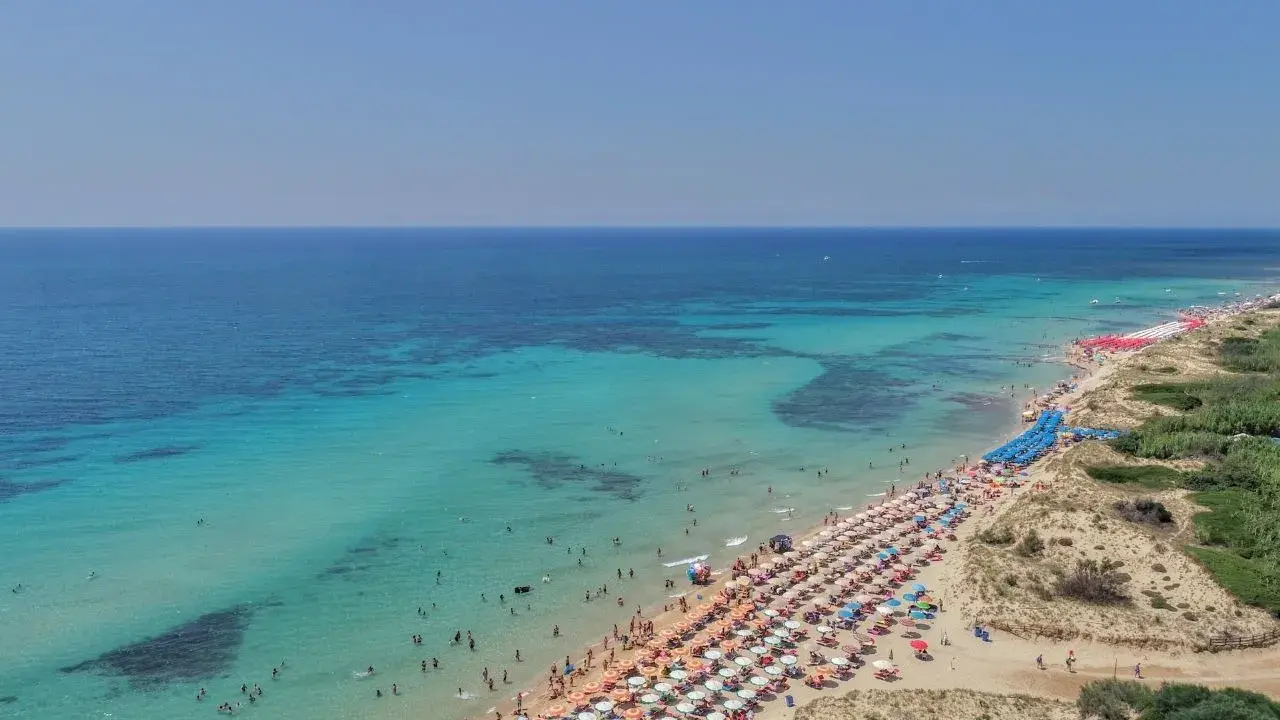 Spiaggia affollata con ombrelloni colorati e acque cristalline, le Maldive della Puglia dove si trovano per godersi il sole e il mare.