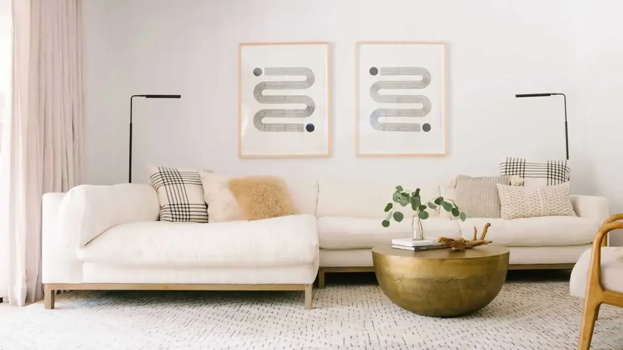 En ljus soffgrupp med en mönstrad matta och ett runt soffbord i mässing. Två grafiska tavlor hänger på väggen.