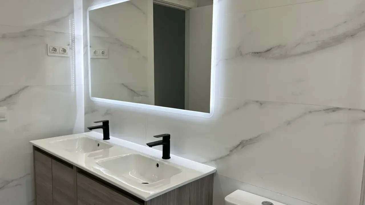 Moderno lavabo doble con grifería negra y espejo iluminado. Una solución ideal para reformar baño sin obras, con un toque de elegancia.