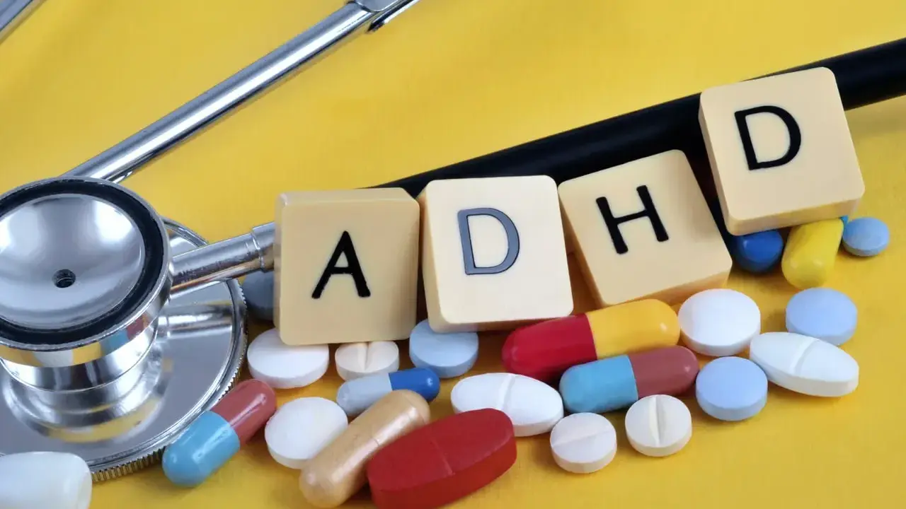Stetoskop i tabletki symbolizujące leki na ADHD. Litery A, D, H, D ułożone na żółtym tle.