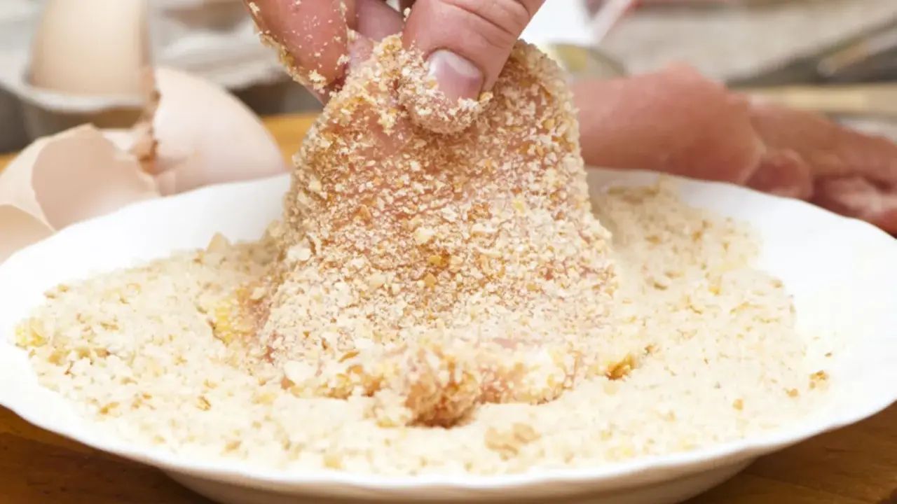Fleisch wird in Paniermehl gewendet. Eine Hand hält das Stück, um es perfekt panieren ohne Ei zu machen.