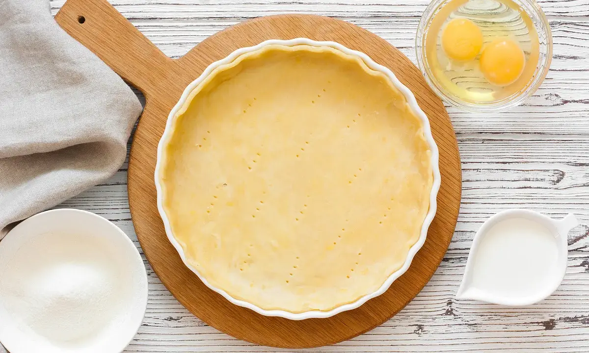 Préparation d'une pâte sucrée pour une tarte. Ingrédients : pâte dans un moule, œufs, sucre, lait.