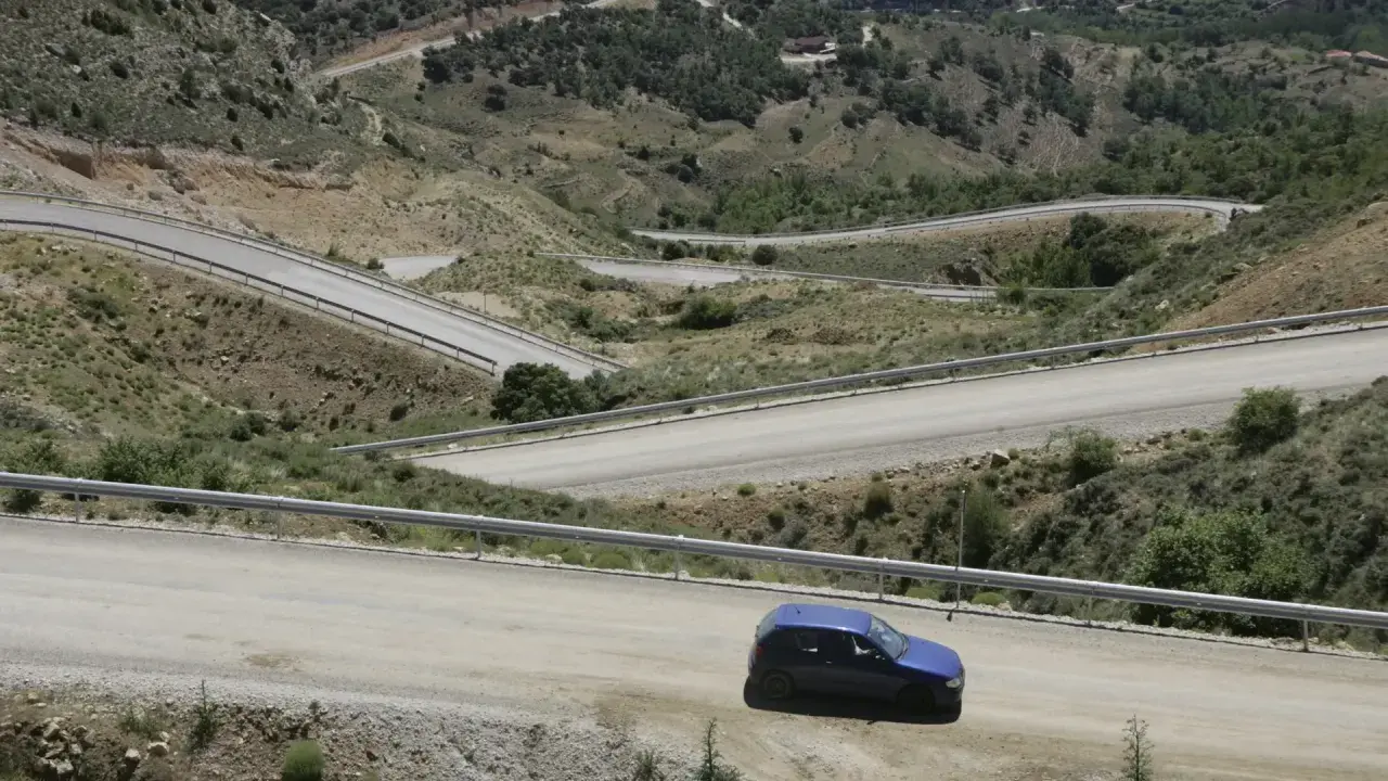 Coche azul en carretera de montaña con curvas pronunciadas. Podría recibir una multa por circular por pista forestal.