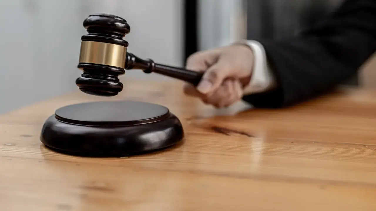 Mano che impugna un martelletto da giudice, pronto a battere sul ceppo. Il suo significato, il g.u.p., è un momento cruciale.