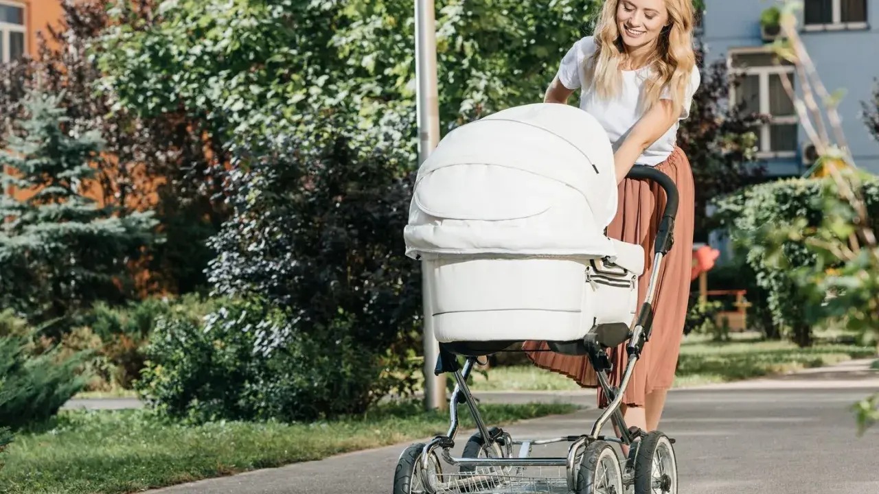 Uśmiechnięta mama spaceruje z białym wózkiem, który jest wyposażony w praktyczne akcesoria.