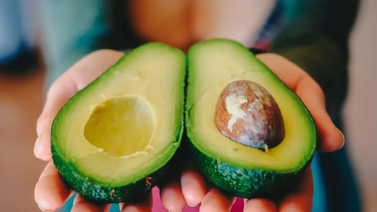 Zwei Hälften einer Avocado werden in Händen gehalten. Eine Hälfte hat den Kern, die andere ist leer. Perfekt, um die Avocado reifen zu lassen.