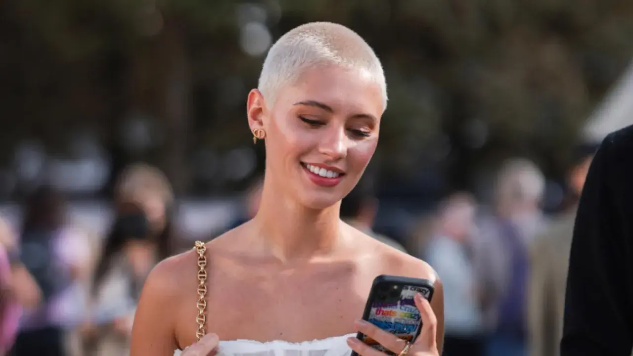Junge Frau mit buzz cut blond, lächelnd und auf ihr Handy schauend.