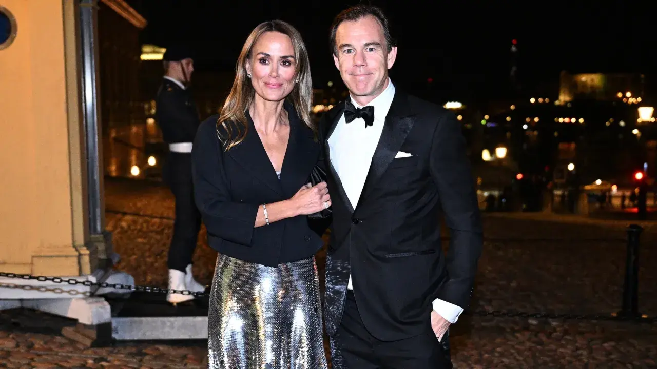 A couple in formal attire poses at night with a blurred city background.