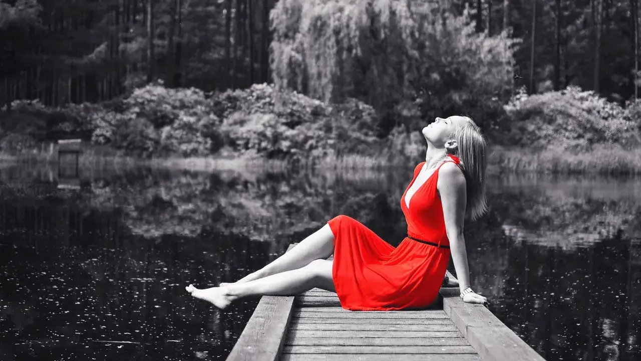 Mujer con vestido rojo sentada en muelle, efecto blanco y negro photoshop.