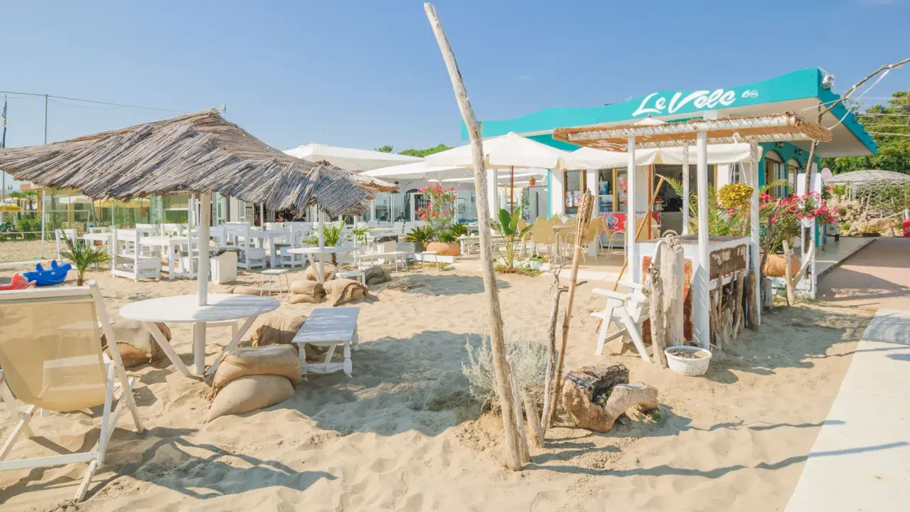 Un angolo di cervia strand con tavoli, sedie e ombrelloni di paglia, pronto ad accogliere i bagnanti.