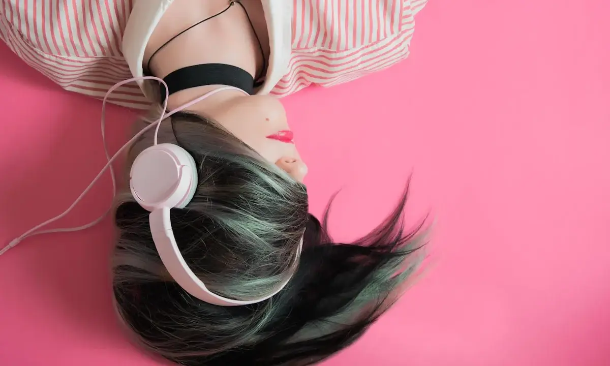 Jeune femme aux cheveux colorés, écouteurs blancs, sur fond rose. Une inspiration pour comment trouver un nom d'artiste.