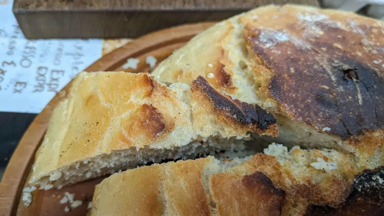 Ein knuspriges, goldbraunes dutch oven brot mit einer luftigen Krume, auf einem Holzbrett serviert.