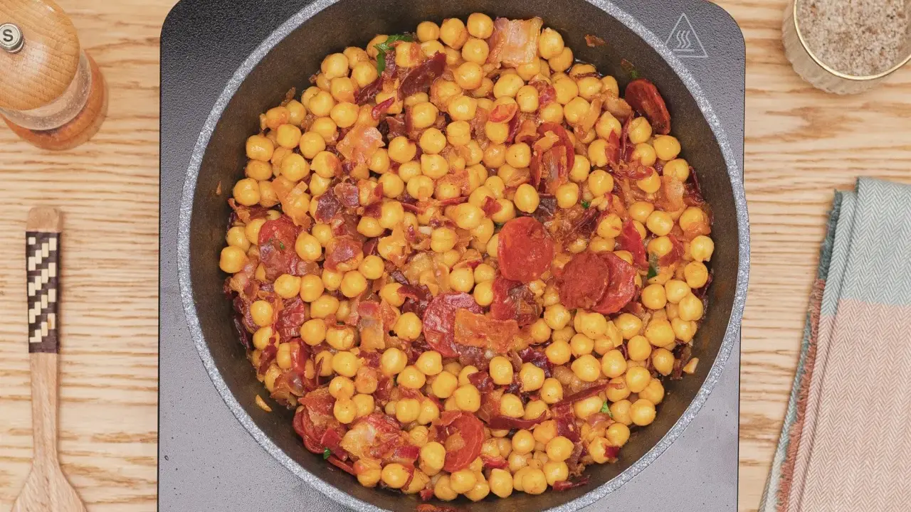Garbanzos fritos con chorizo y bacon en sartén, listos para servir. Un plato sabroso y reconfortante.