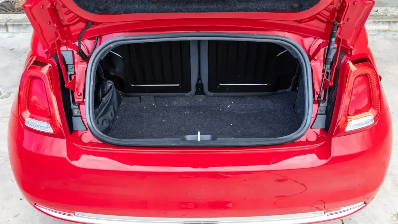 Maletero abierto de un Fiat 500 rojo, mostrando el espacio de carga cubierto de fieltro oscuro.