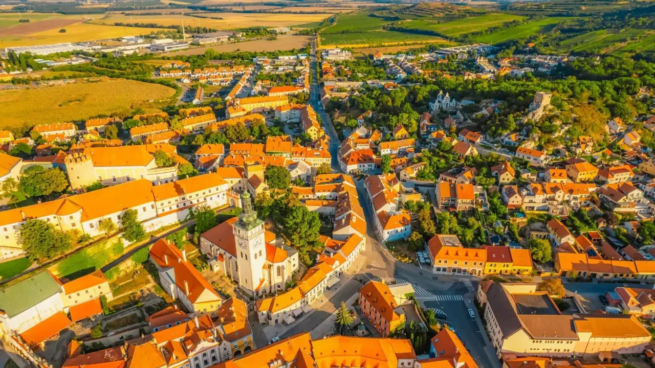 Malownicze miasteczko na Morawach w Czechach, z dominującą wieżą kościelną i pomarańczowymi dachami, otoczone zielonymi wzgórzami.