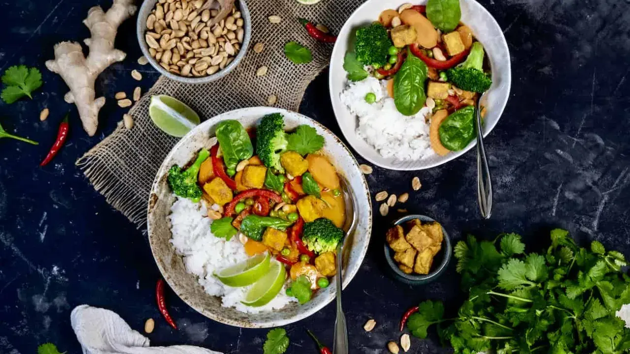 Zwei Schüsseln mit Reis, Tofu, Brokkoli und Erbsen. Ein Gericht, das vegan und proteinreich ist, mit Ingwer, Chili und Koriander garniert.