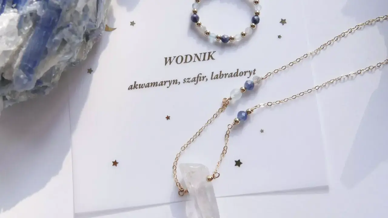 Złoty naszyjnik z kryształem górskim i kamieniami, idealny talizman dla Wodnika. Obok pierścionek z akwamarynem, szafirem i labradorytem.