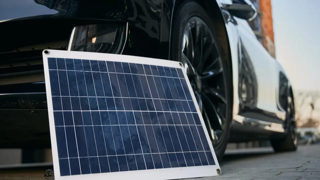 Panel solar portátil junto a un coche eléctrico, listo para cargar en casa.