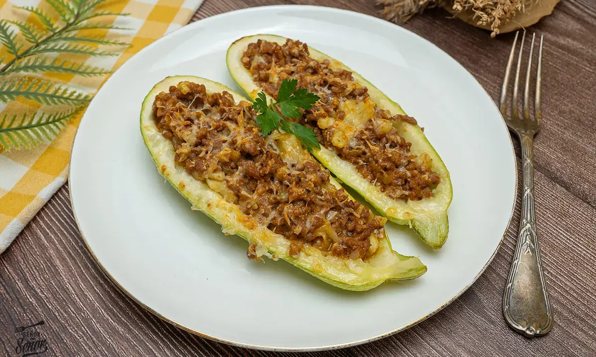 Dos mitades de calabacines rellenos de carne picada y queso gratinado, decorados con perejil. Un plato casero y delicioso.