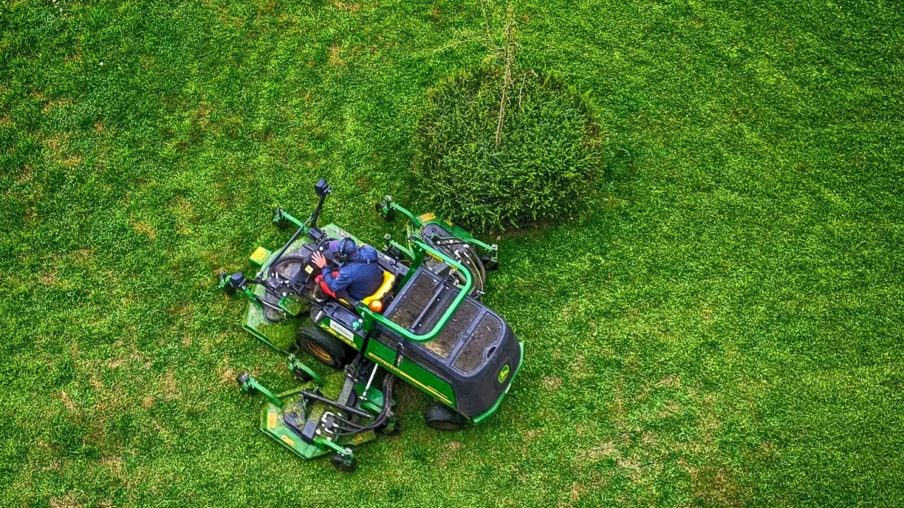 Un homme est assis sur un tracteur tondeuse, prêt à passer la tondeuse le dimanche. L'herbe est d'un vert éclatant.
