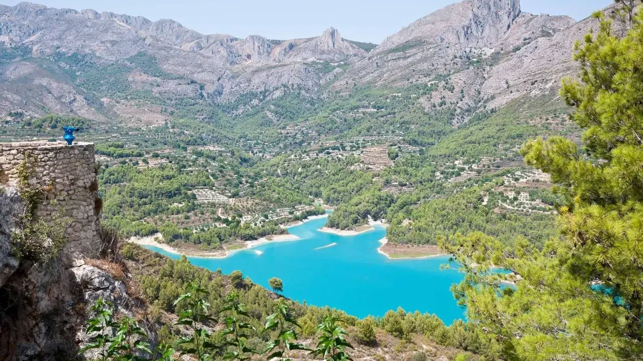 Espectacular vista de la ruta pueblos interior Alicante, con un embalse turquesa rodeado de montañas y vegetación.