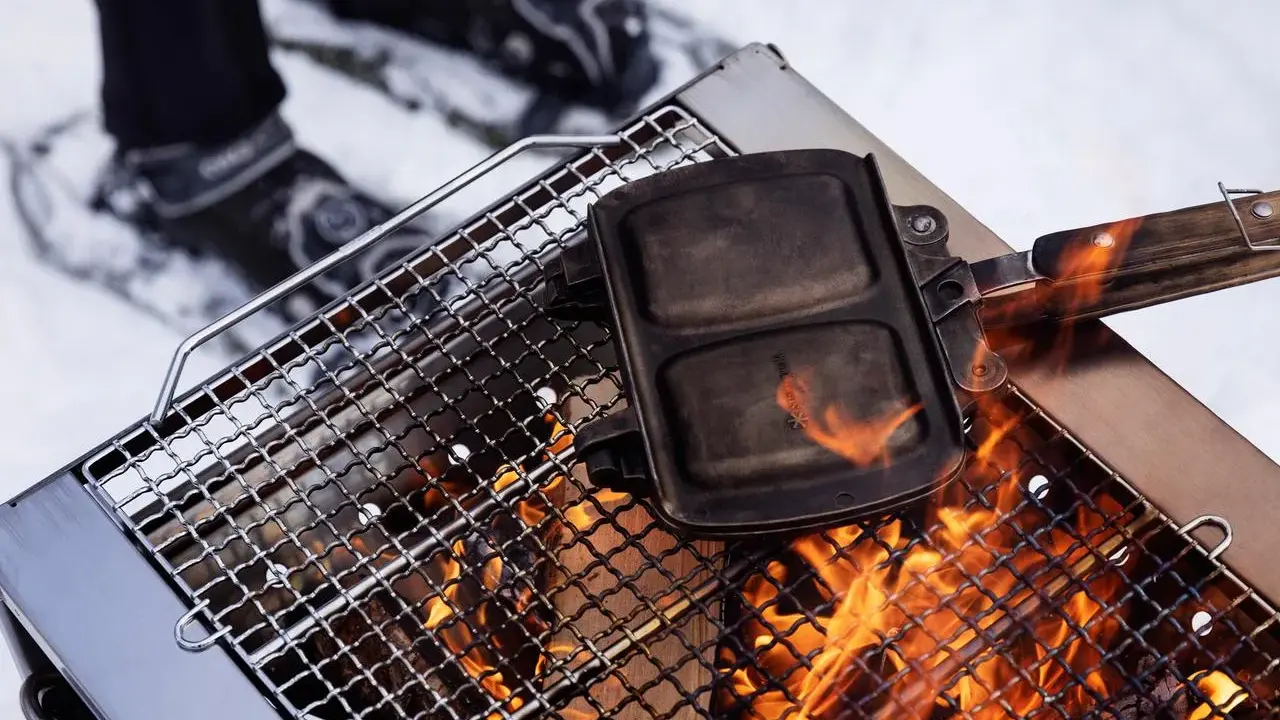 En smörgåsgrill värms över en eld, perfekt för friluftsmat recept i snön.