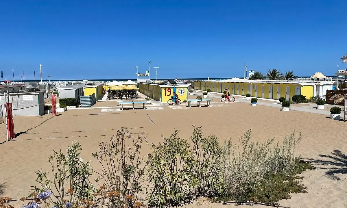 Spiaggia di Riccione con cabine gialle e blu, tavoli da ping pong e bambini in bicicletta al Bagno 19.