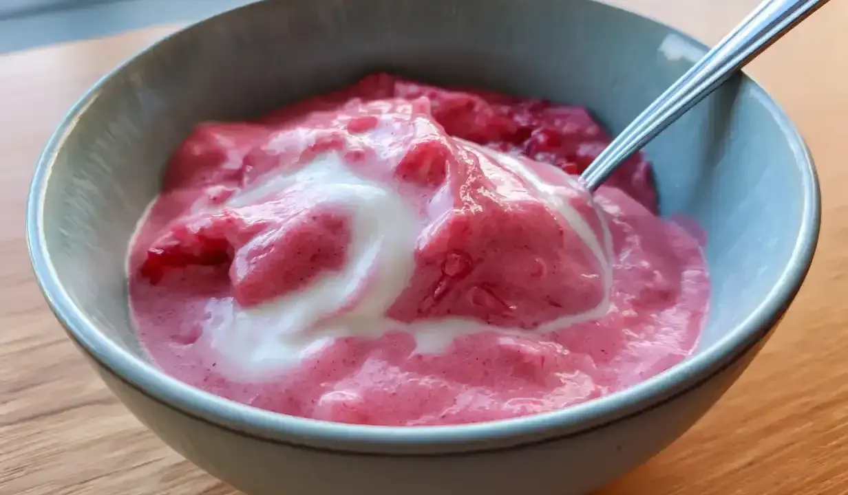 En skål med krämig rabarbercurd med en virvel av grädde. Perfekt för en somrig fika.