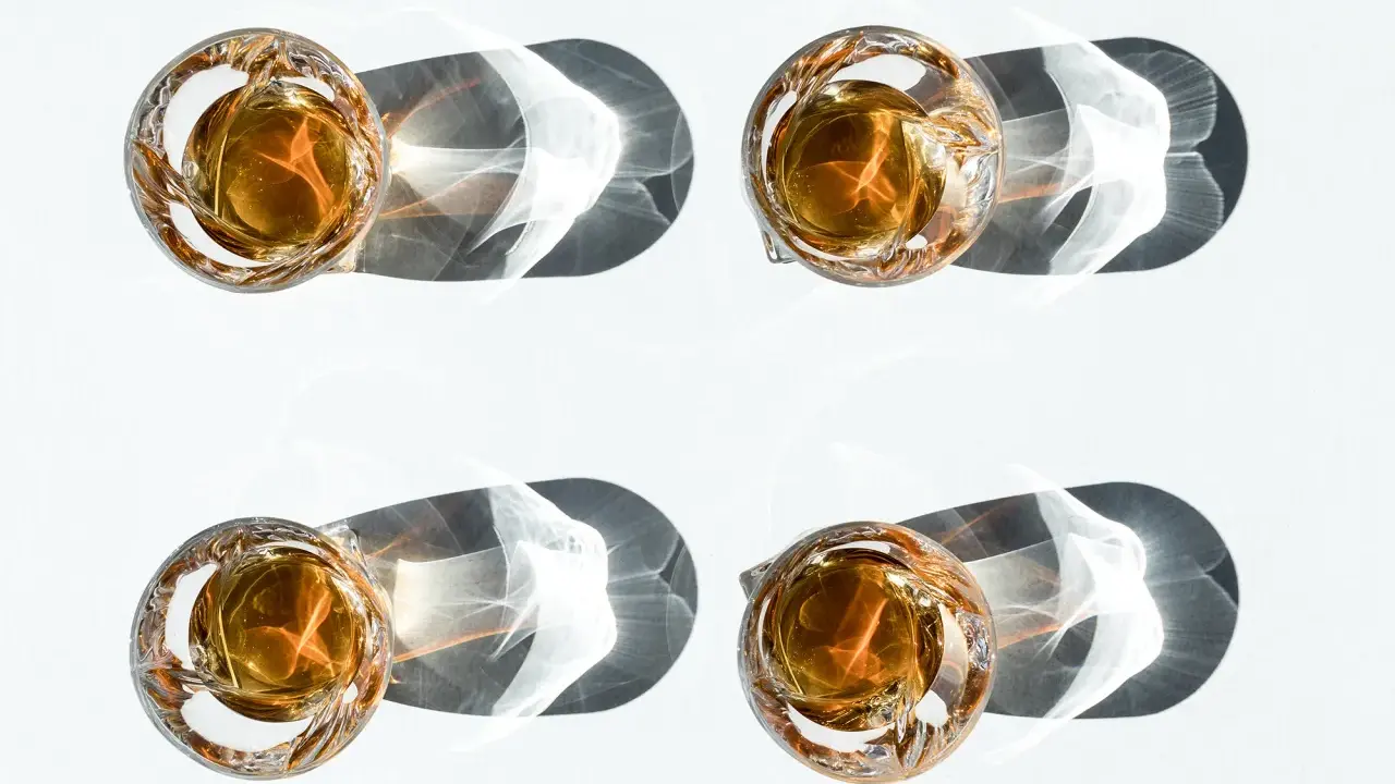 Vier Gläser mit bernsteinfarbenem Whiskey, die im Sonnenlicht stehen. Ein Vergleich zwischen Bourbon vs. Whiskey.