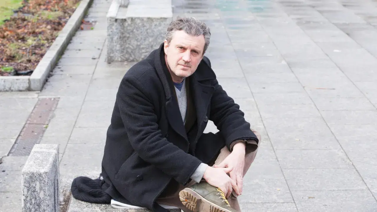 Uomo con cappotto nero seduto all'aperto, ricorda le atmosfere dei rocco schiavone libri.