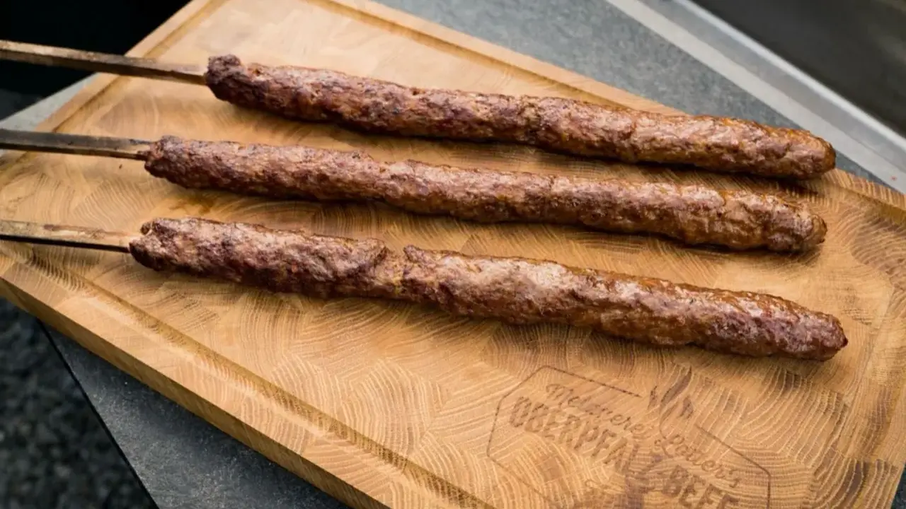 Drei saftige Adana Kebap Spieße liegen auf einem Holzbrett. Perfekt für ein authentisches Adana Kebap Rezept.