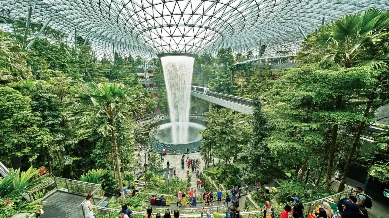 Imponerande vattenfall och frodig grönska under glastaket på singapore flygplats. Människor njuter av den unika miljön.