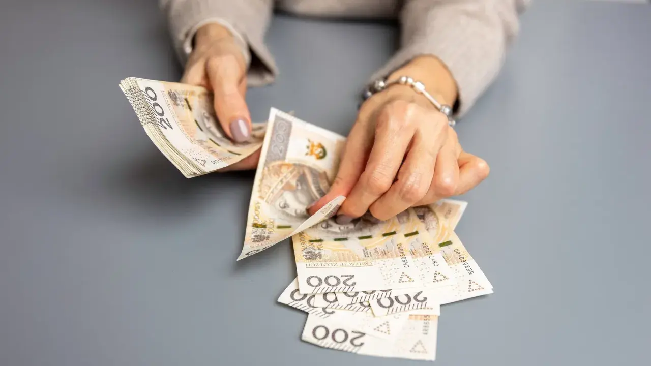 Dłonie liczą banknoty 200 zł. To może być wypłata świadczenia urlopowego na wymarzone wakacje.