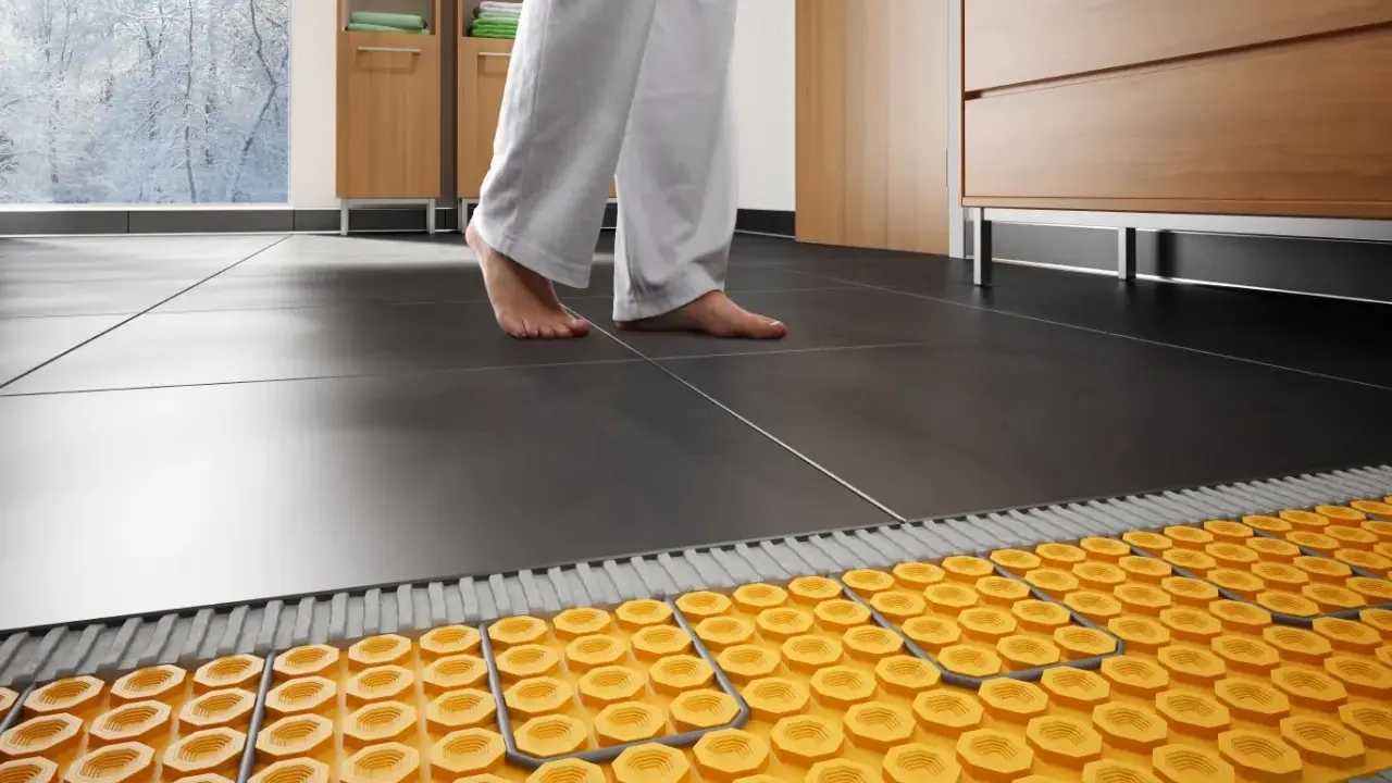 Piedi nudi su piastrelle scure, con un sistema di riscaldamento a pavimento visibile sotto. Addio termosifoni, benvenuta comodità!