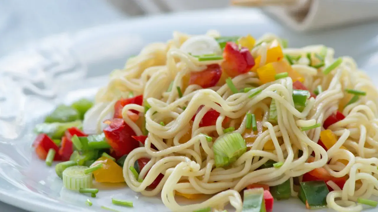 Ein bunter asia nudelsalat mit Paprika und Frühlingszwiebeln auf einem weißen Teller.