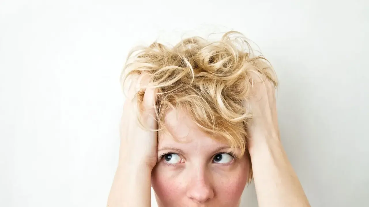 Kobieta z blond włosami, trzymająca się za głowę, z wyrazem zamyślenia i niepokoju, jakby doświadczała wahań nastroju związanych z cyklotymią.