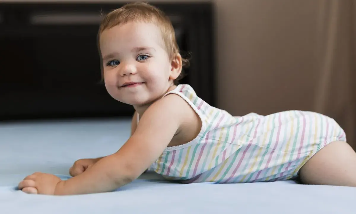 Un adorabile neonato di 8 mesi, con occhi azzurri e un sorriso contagioso, gioca sul letto.