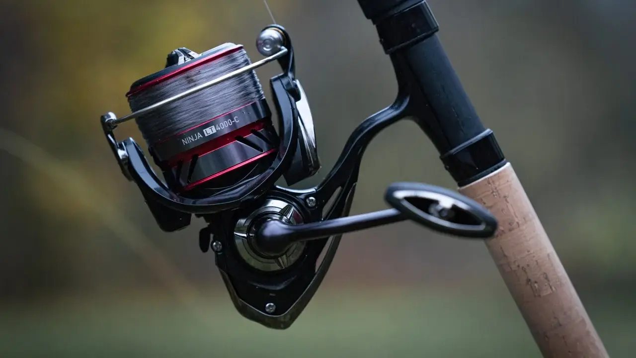 Czarne, nowoczesne detale budowy kołowrotka wędkarskiego Daiwa Ninja LT 4000-C z szarą żyłką i korkową rękojeścią.
