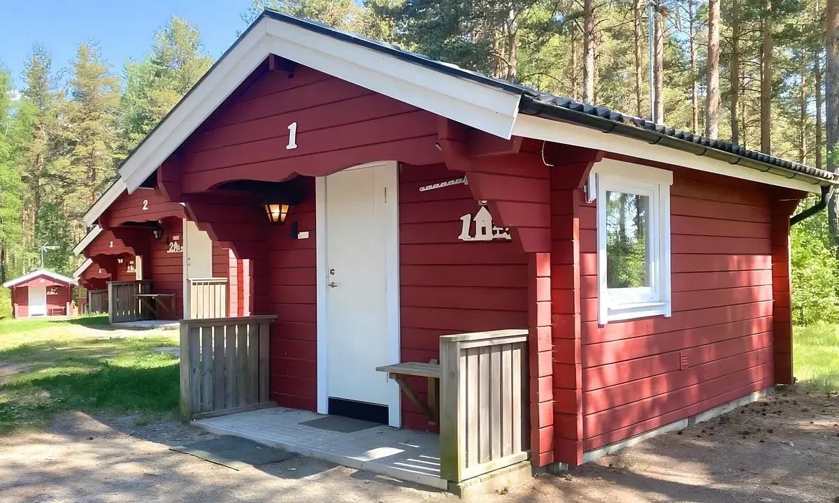 Röda stugor med vita knutar vid Gränna camping. En vit dörr och ett fönster syns på stuga nummer 1.
