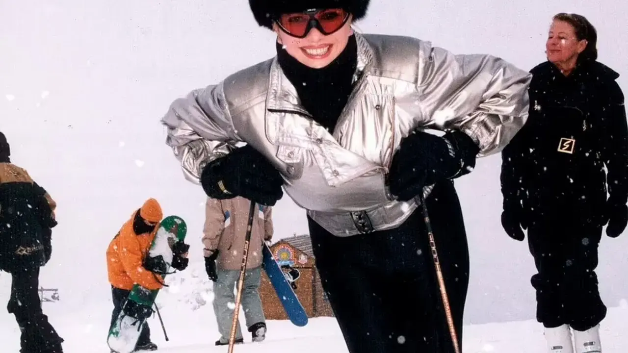 Ivana Trump joven, sonriendo y esquiando con un gorro de piel y gafas de esquí. A su alrededor, otras personas disfrutan de la nieve.