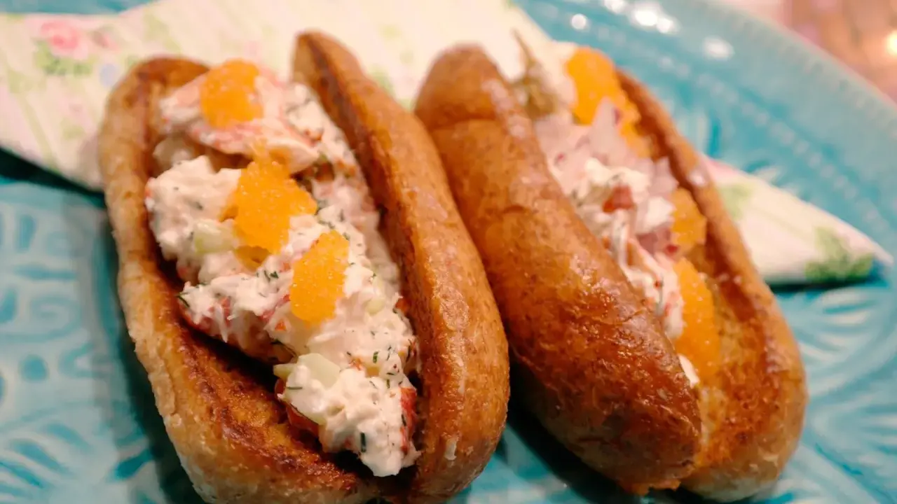 Två lyxiga lobster rolls med krämig fyllning, krispig gurka och orange rom på ett turkost fat.