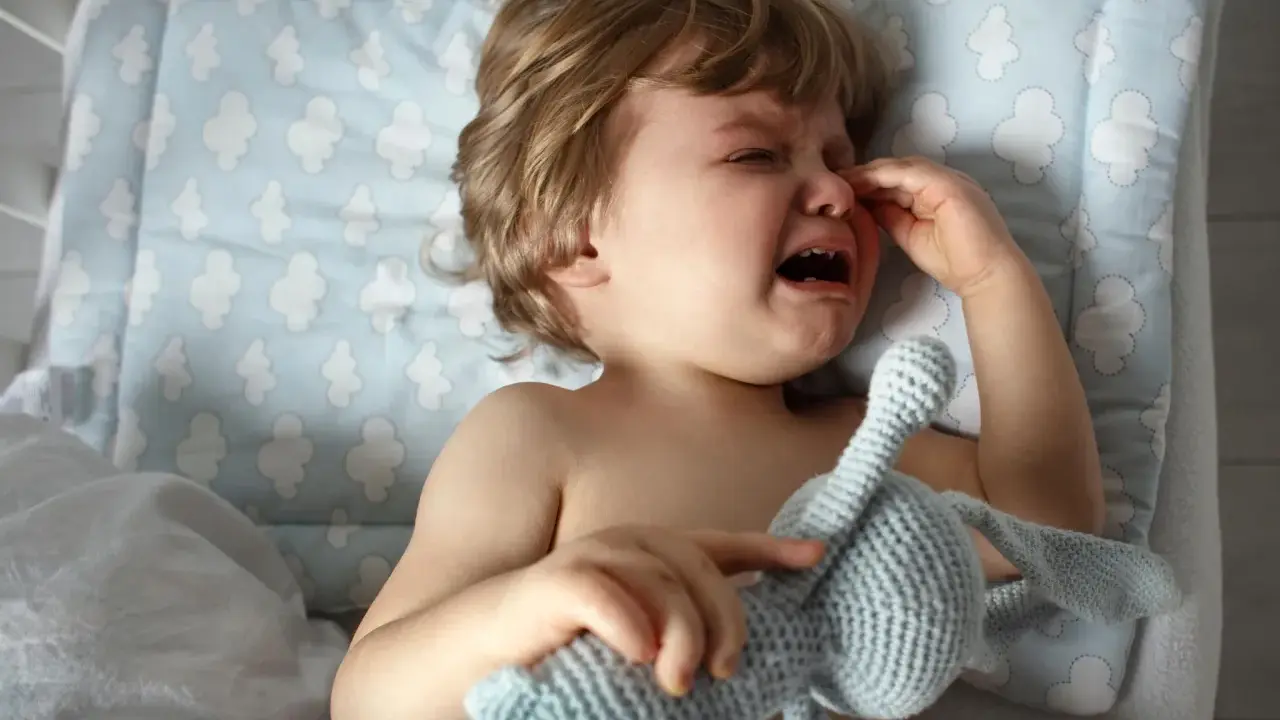 Kleines Kind weint im Schlaf, hält seinen Kuschelhasen fest. Tränen laufen über die Wangen, ein trauriger Moment.