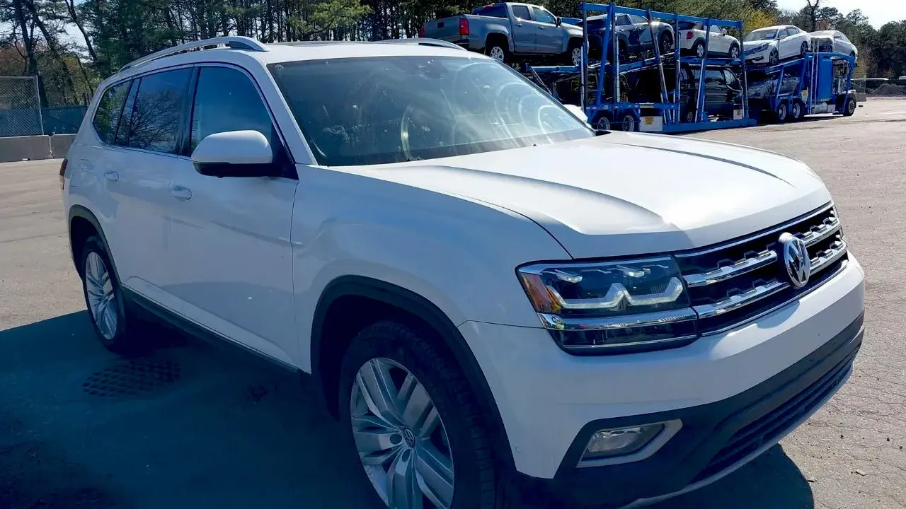 Biały VW Atlas stoi na parkingu, w tle widać lawetę z innymi samochodami.