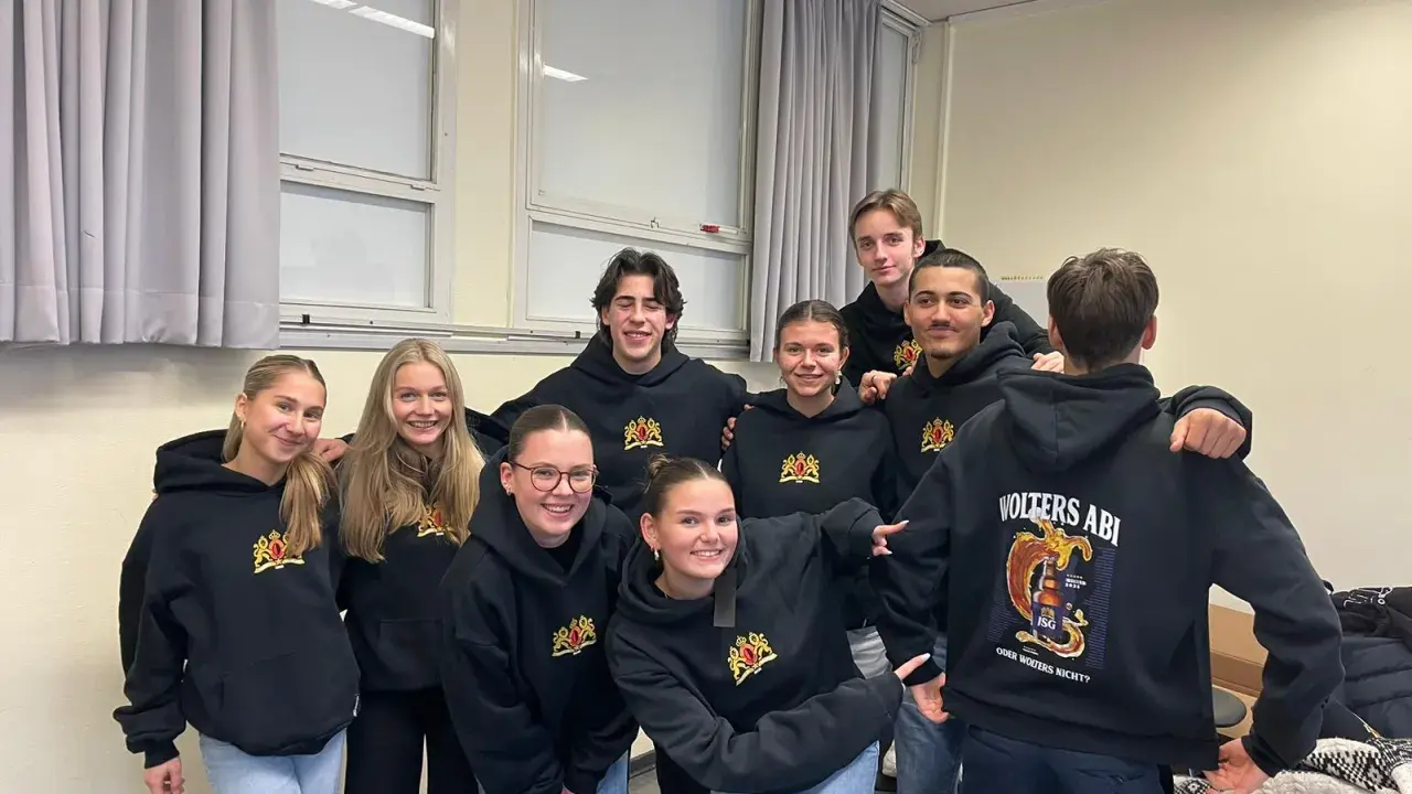Acht lächelnde Schüler in schwarzen Hoodies mit dem Aufdruck "Volters Abi". Wie nennt man das Abitur noch?