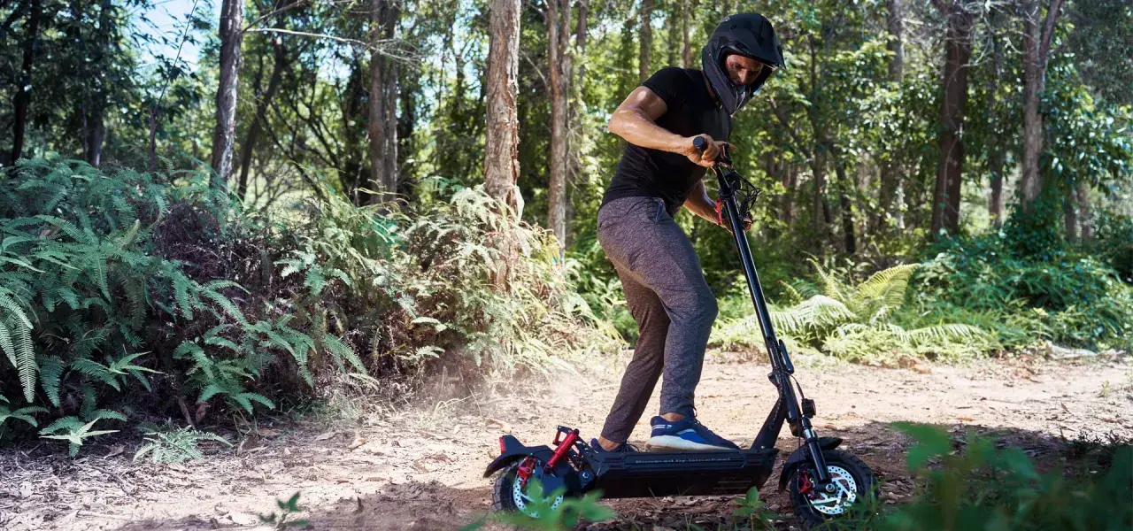 Un homme en casque roule en trottinette électrique dans une forêt. Il semble rencontrer un problème, peut-être un code erreur e8 trottinette électrique.