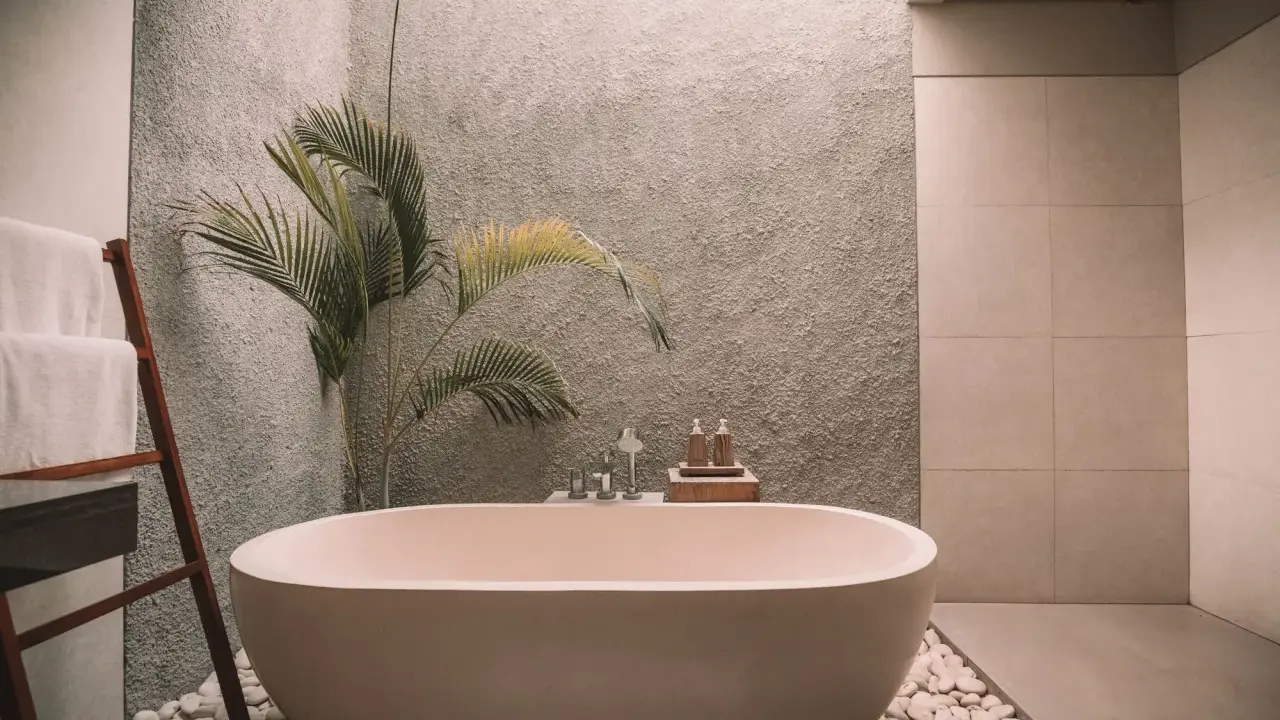 Relajante bañera exenta rodeada de piedras blancas, toallas dobladas en una escalera de madera y una planta tropical. Un ejemplo de cuartos de baño modernos y serenos.